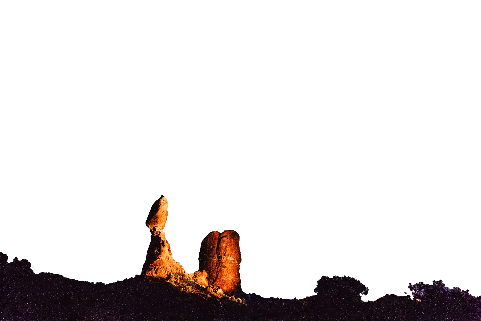 Two illuminated rock formations at night against a pitch-black sky.